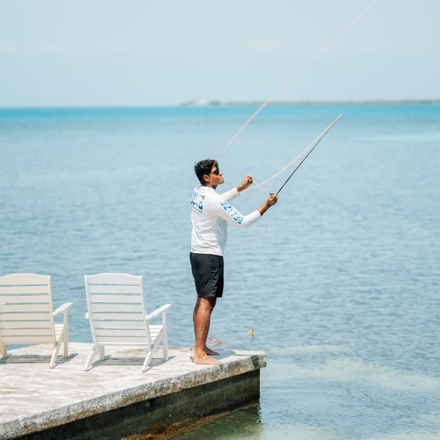 A man stands on a pier, casting a fishing line into the water.