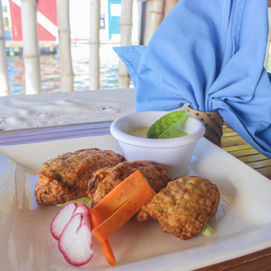 A plate of three fried appetizers accompanied by a dipping sauce and colorful vegetable garnishes.