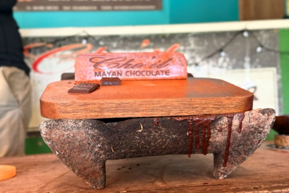 A wooden platform with a chocolate block labeled "Mayan Chocolate" sits atop a stone base, with chocolate dripping down the sides.