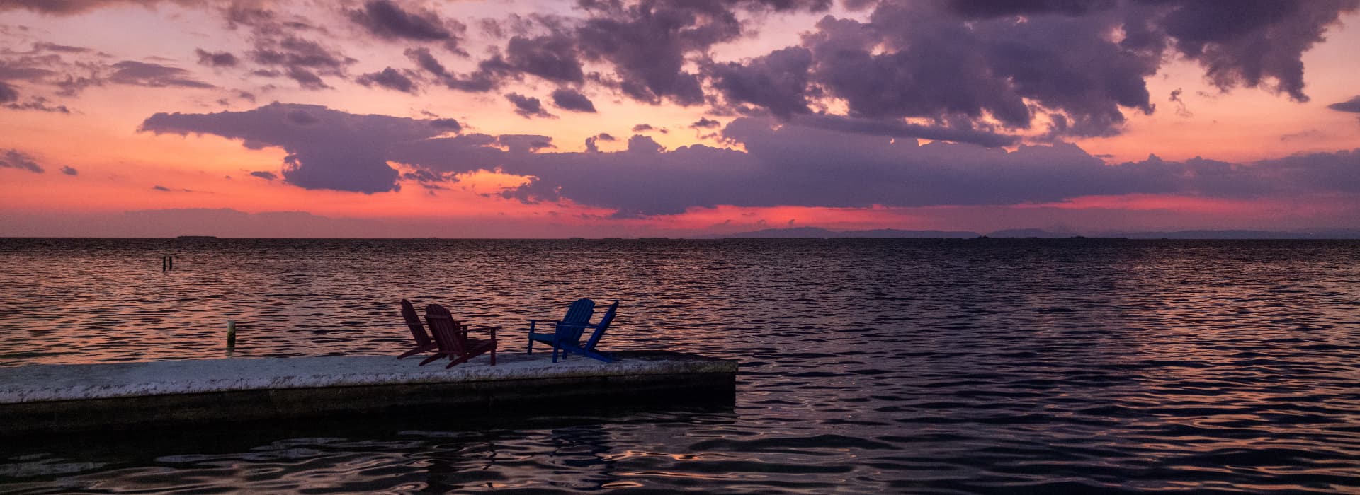 Two colorful chairs on a dock overlooking a tranquil sea at sunset.
