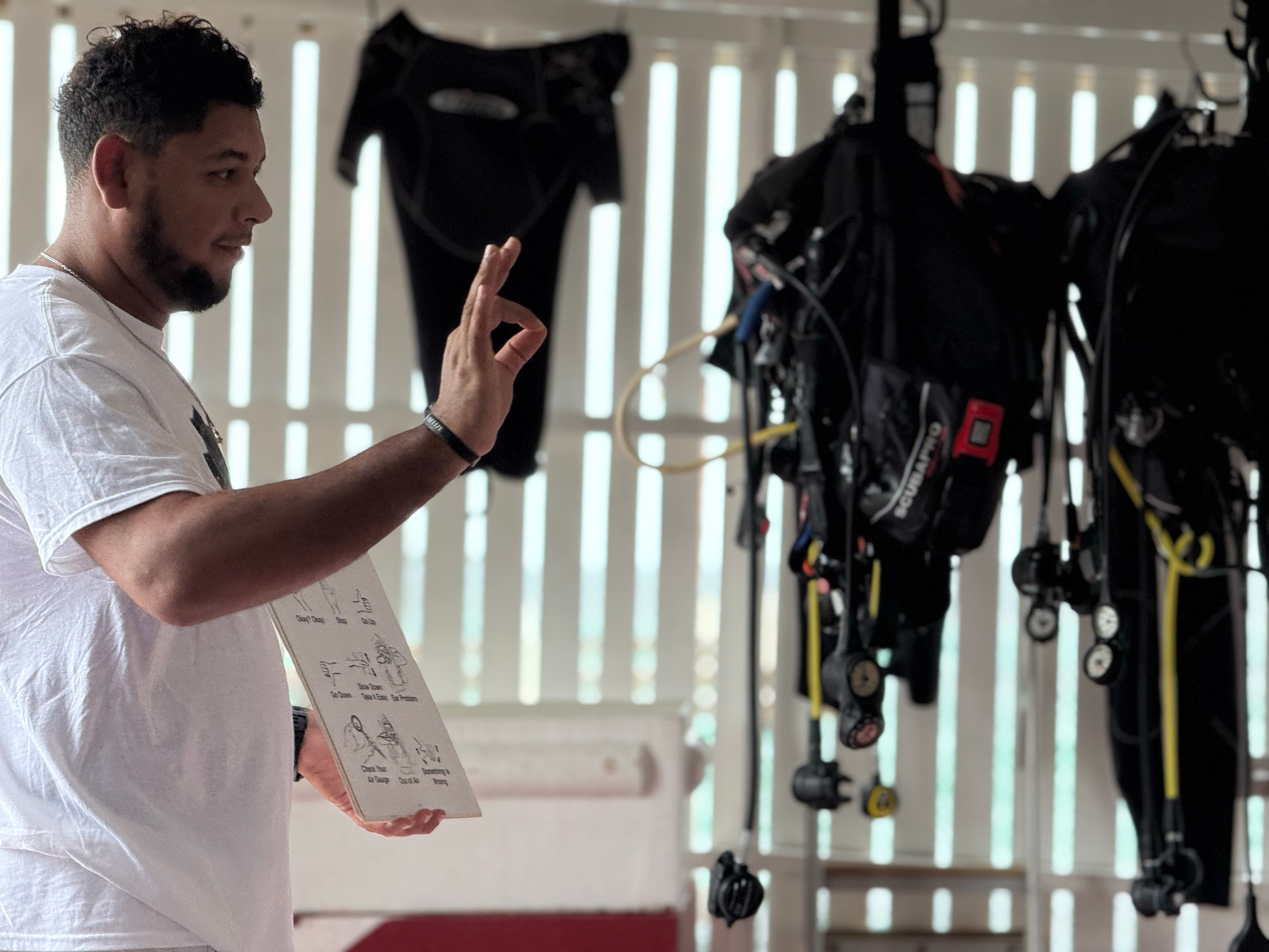 A man demonstrates scuba diving techniques while holding a whiteboard in a training area.