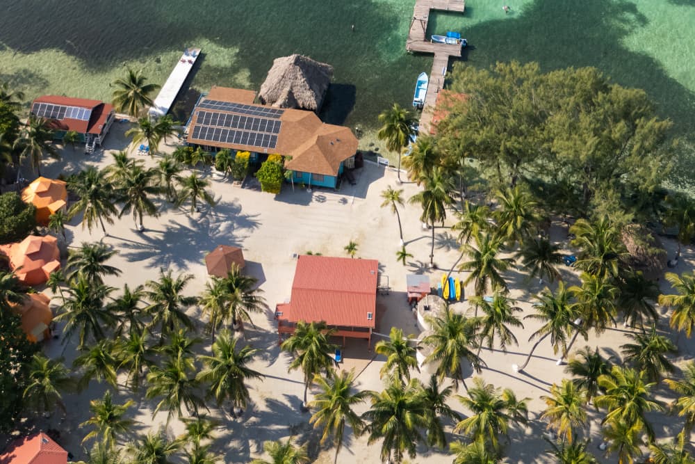 Aerial view of a beach resort with palm trees, colorful cabanas, and a dock extending into clear waters.
