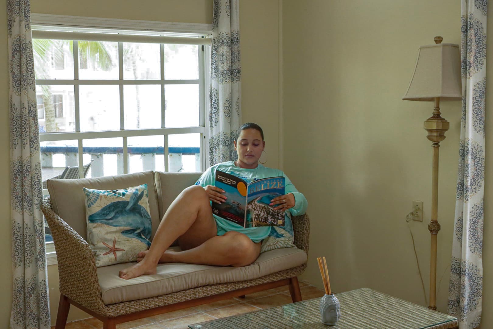 A woman sits on a couch reading a travel magazine in a bright, cozy room.