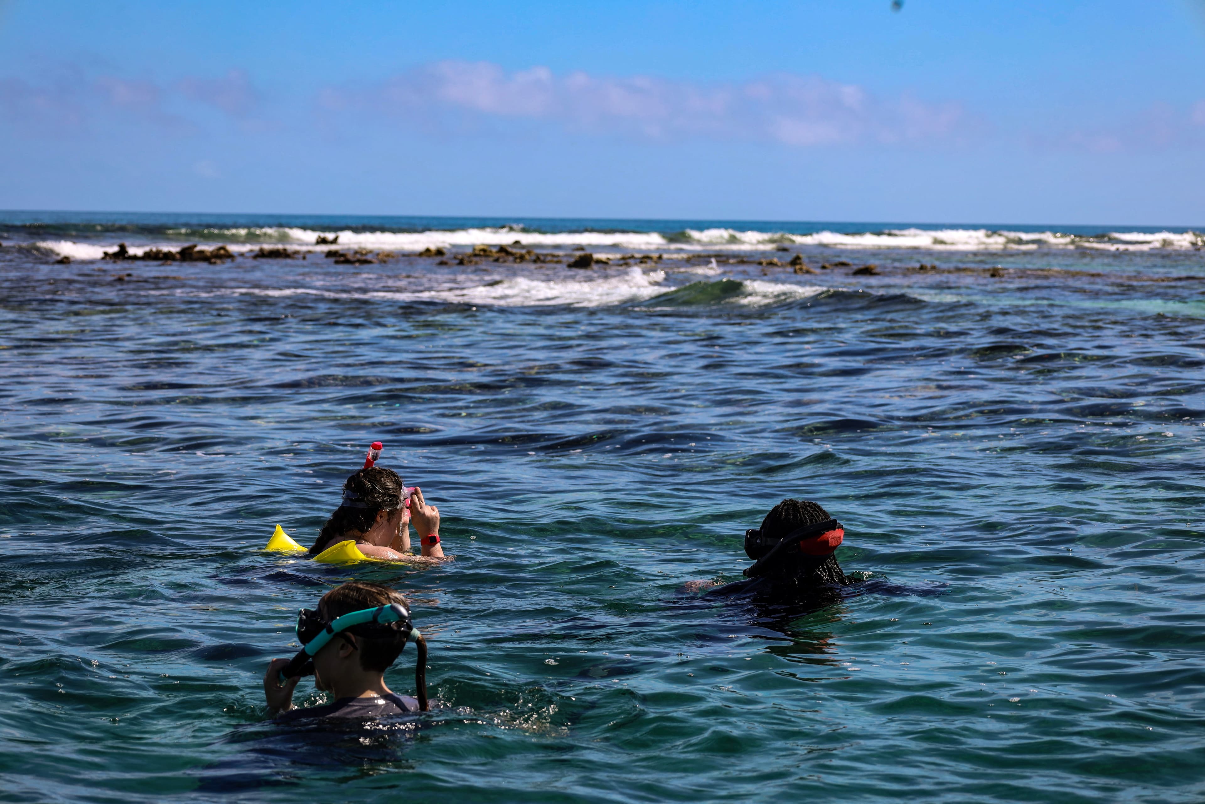 Three people are snorkeling in a clear ocean with gentle waves.