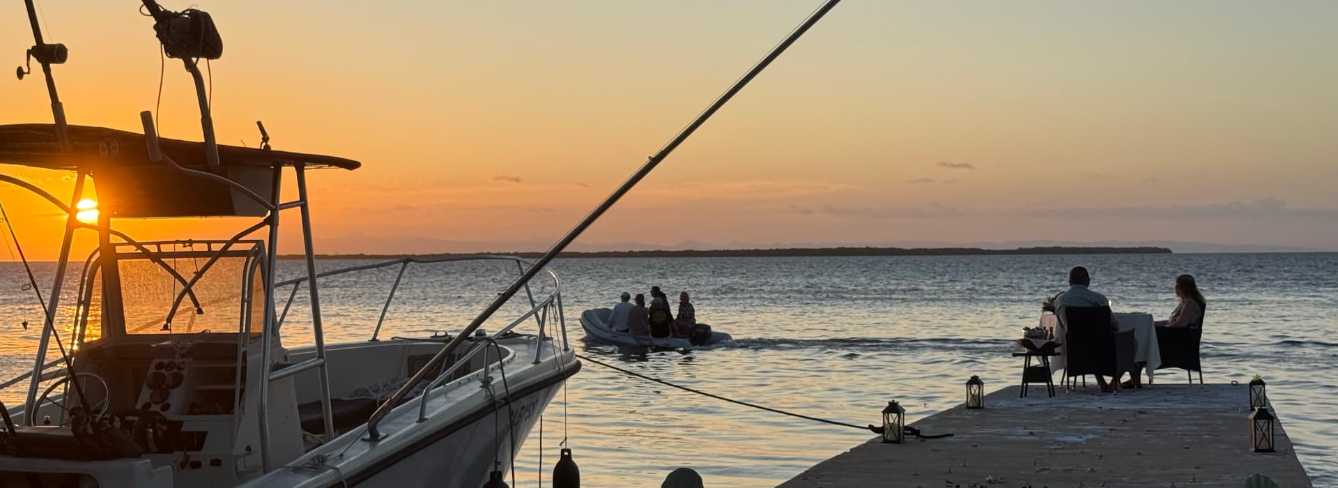 A sunset view over a calm sea with a dock and a boat in the foreground.