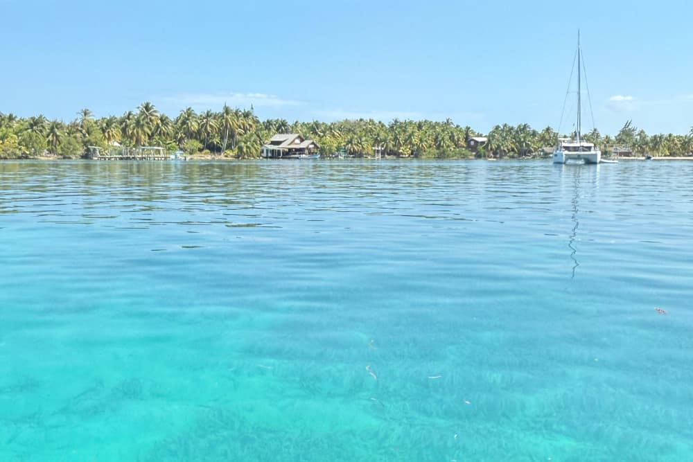Calm turquoise waters with a sailboat and tropical greenery in the background.