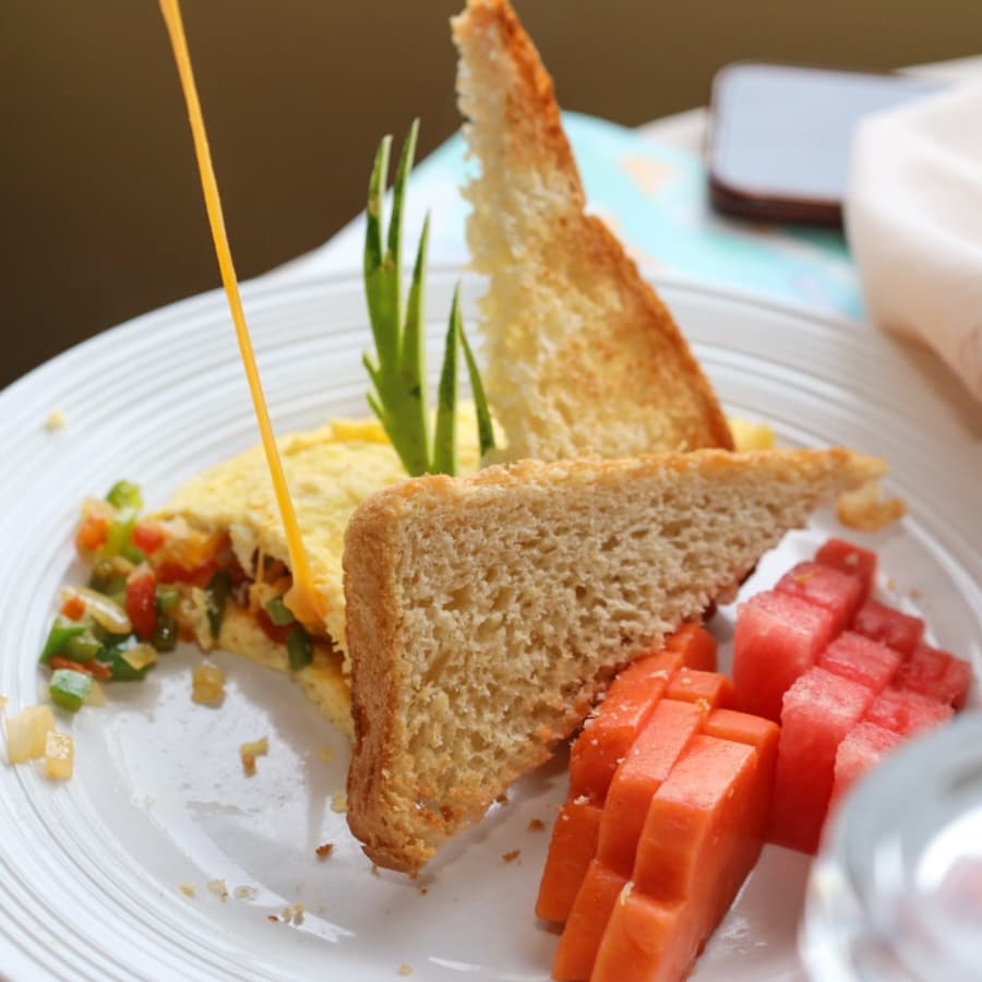 A plate featuring a fluffy omelet garnished with vegetables, two slices of toasted bread, and colorful diced watermelon and papaya.