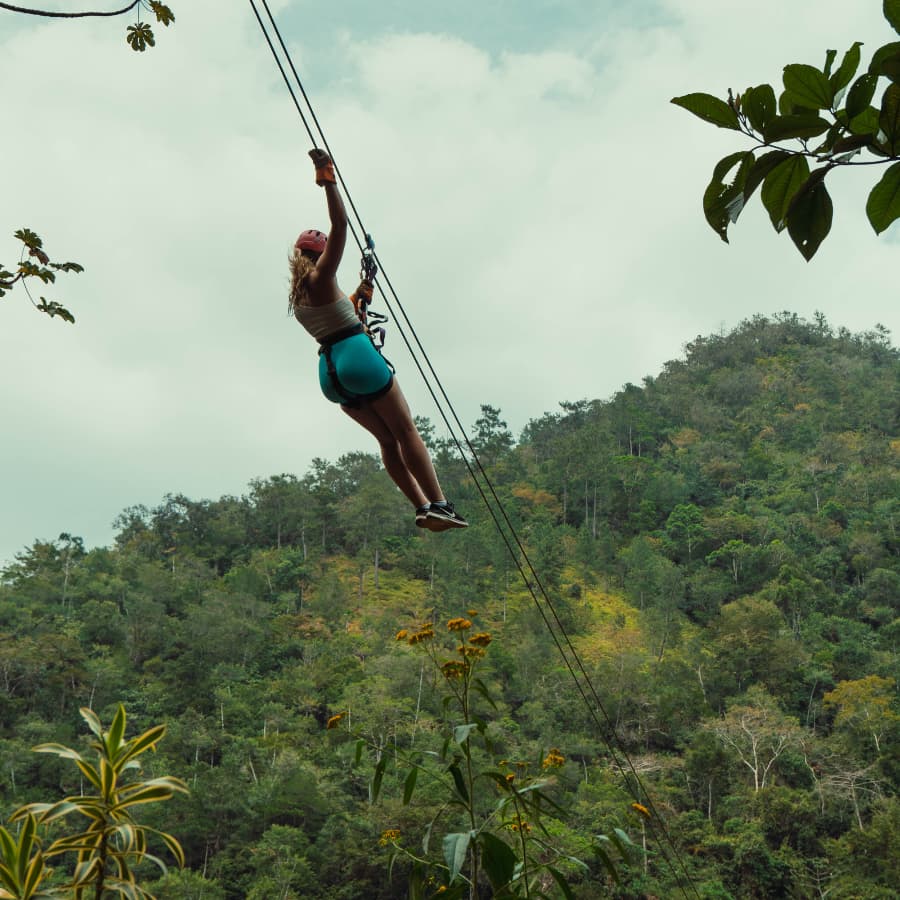 A person zip-lining over a lush green hillside.
