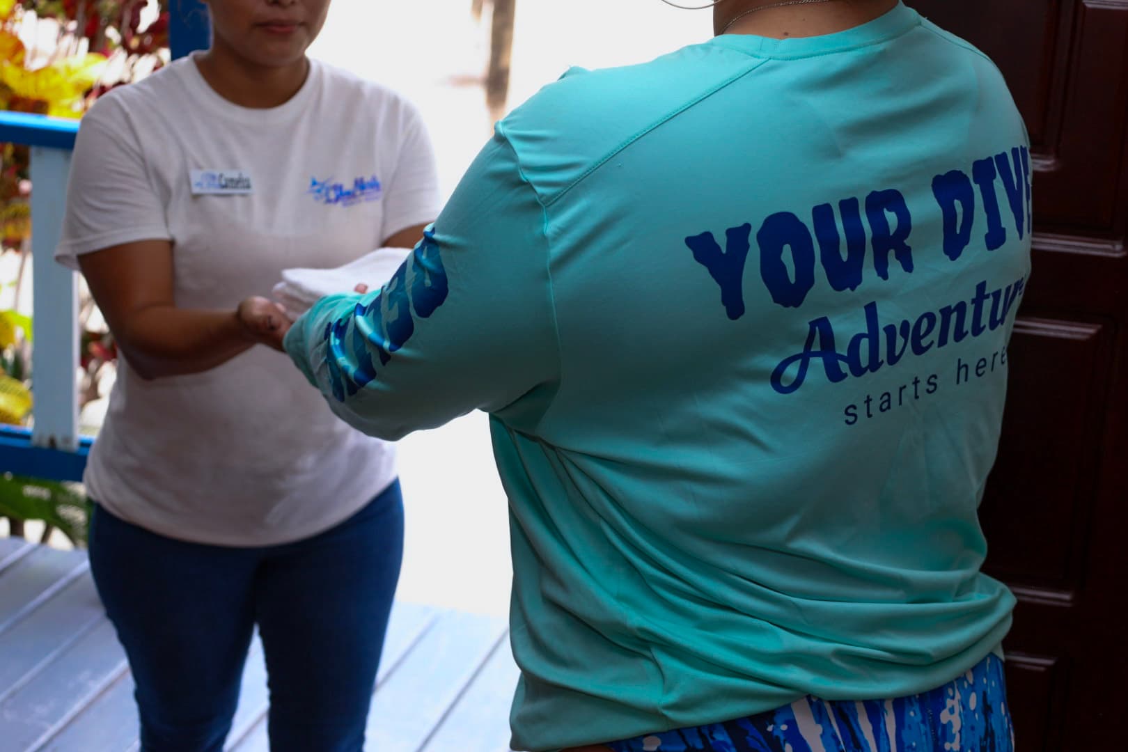 A person in a blue shirt hands a towel to another person at a doorway.
