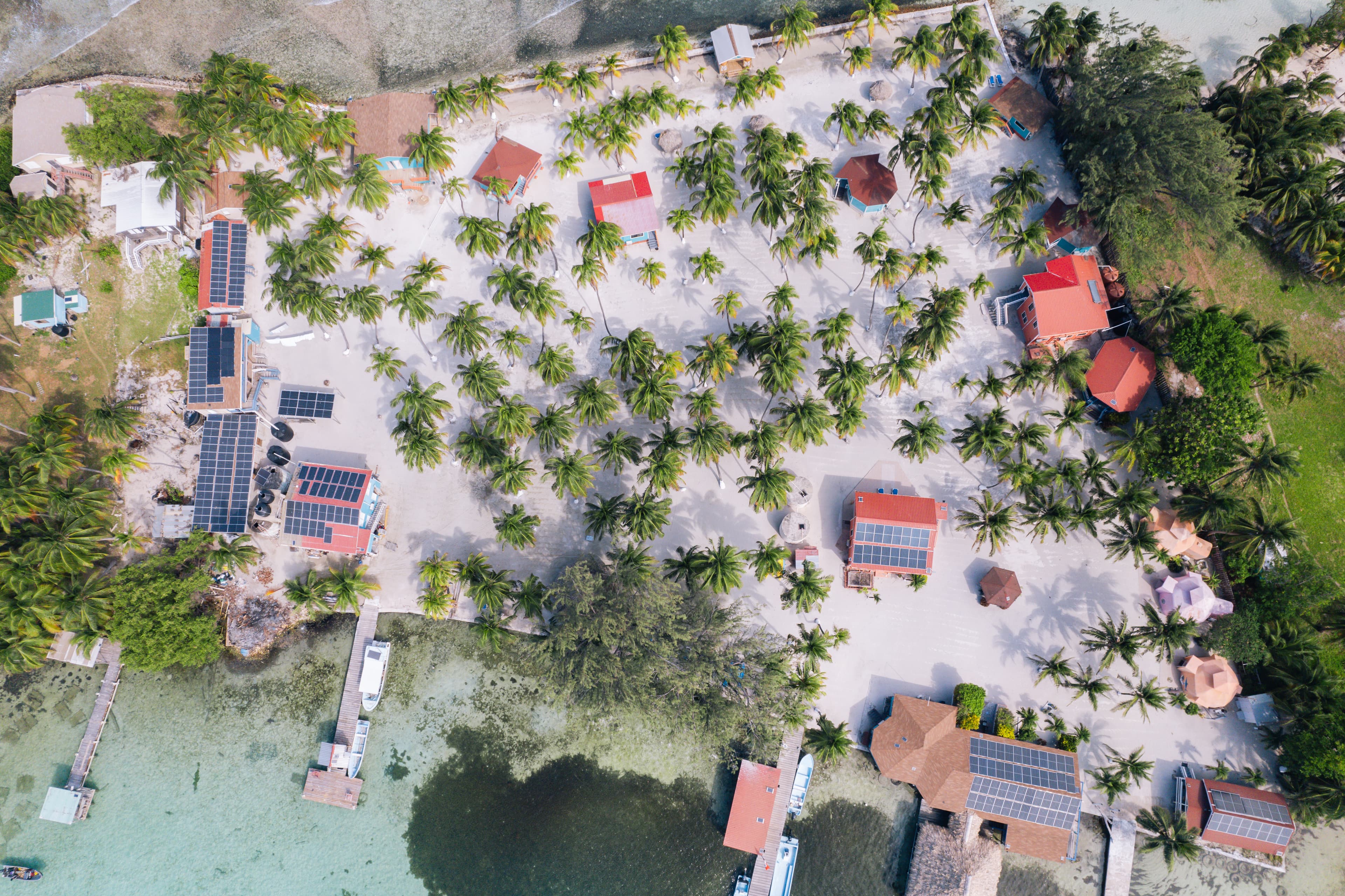 Aerial view of a beachfront resort surrounded by palm trees and solar panel installations.