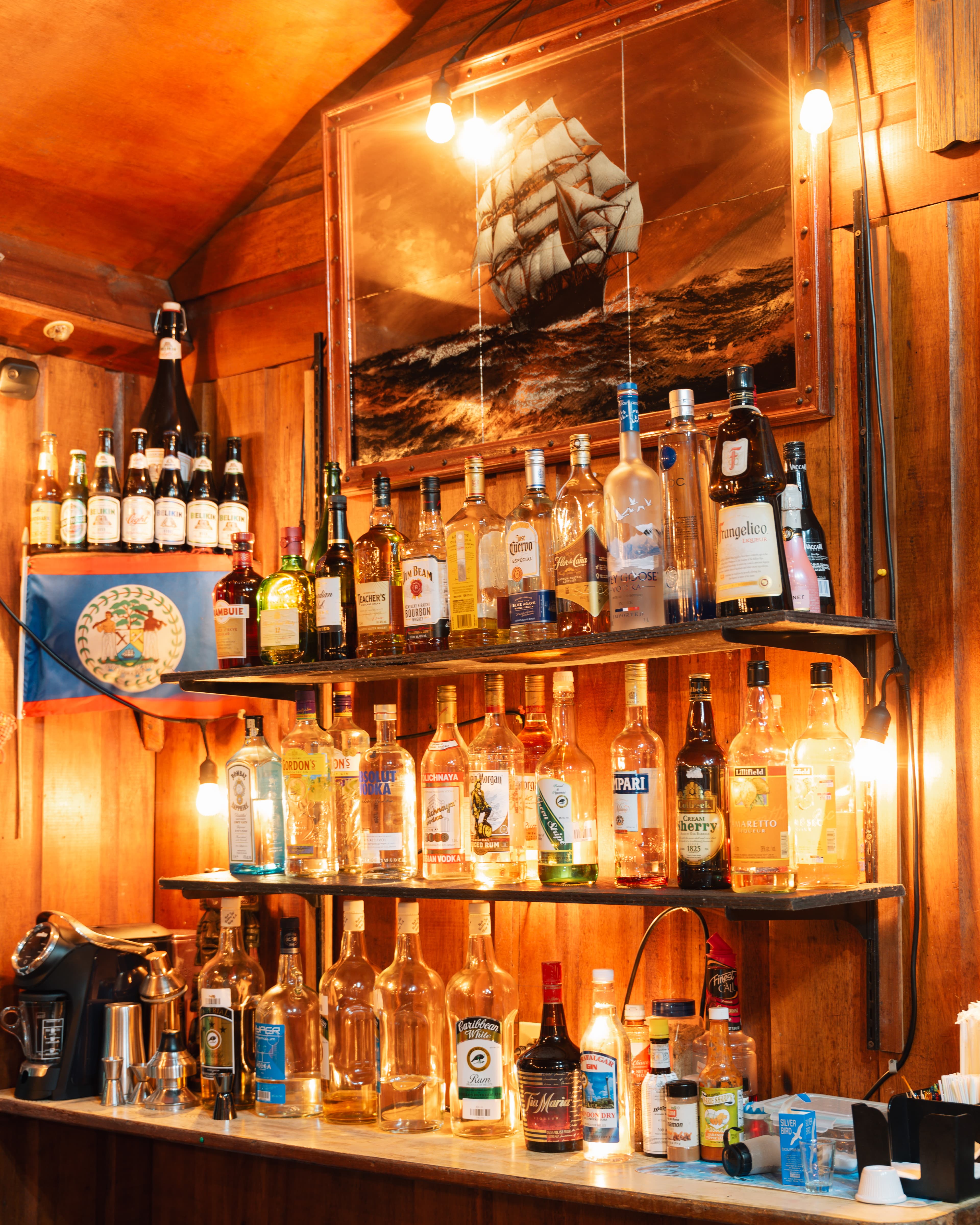 A well-stocked bar featuring various bottles of spirits and a ship painting on the wall.