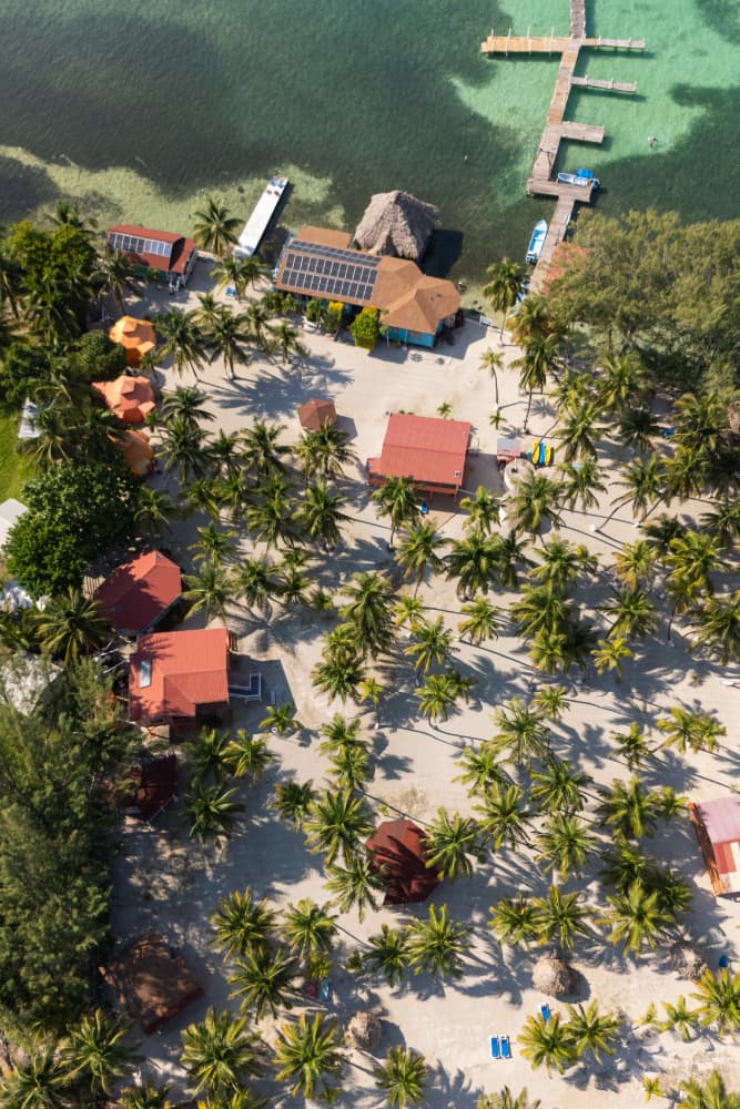 Aerial view of a tropical beach resort with palm trees, colorful huts, and a wooden pier.