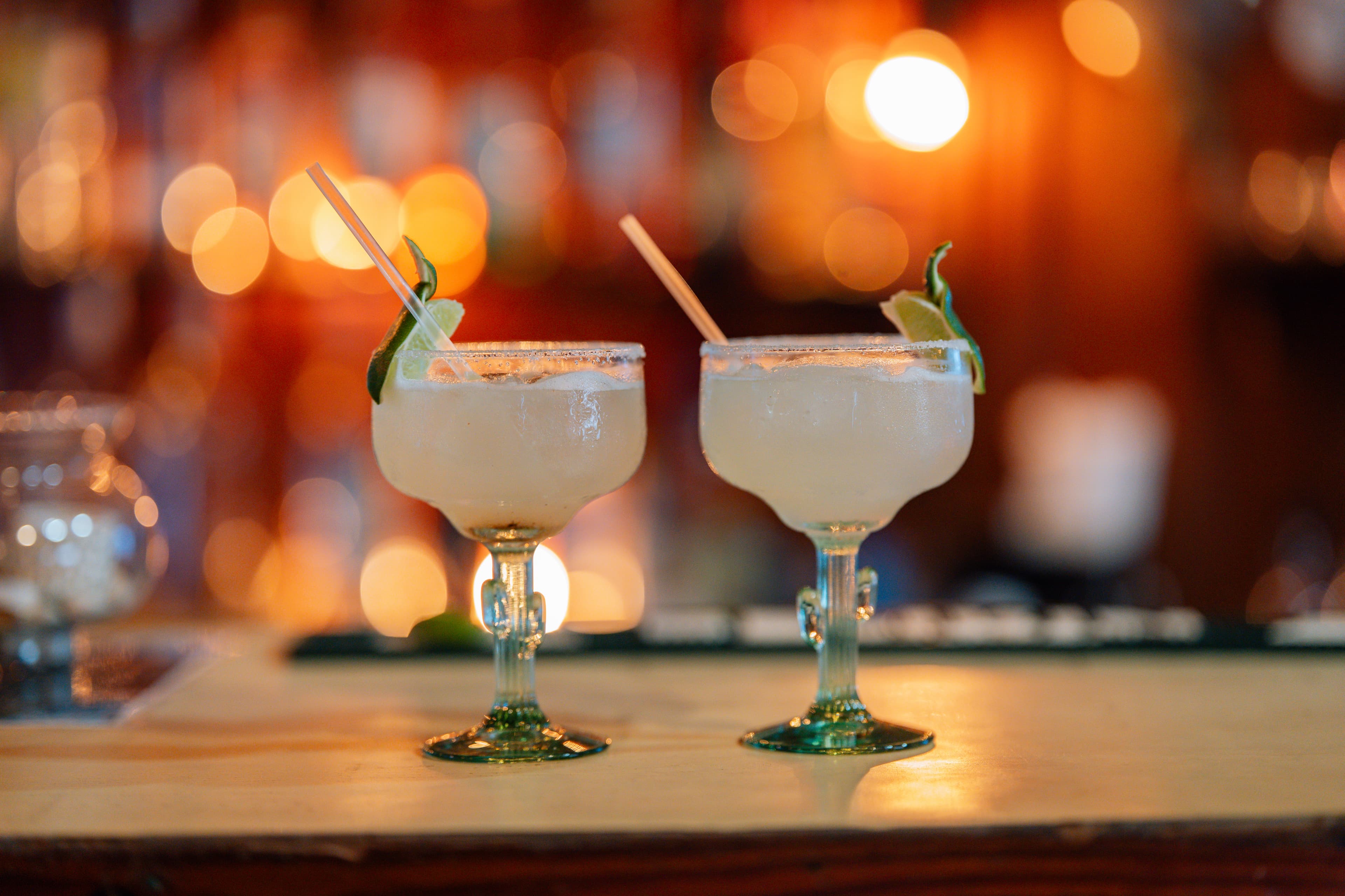 Two margarita cocktails with lime garnishes on a bar.