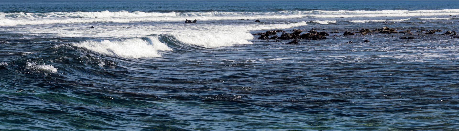 Waves gently roll over a rocky shoreline under a clear sky.