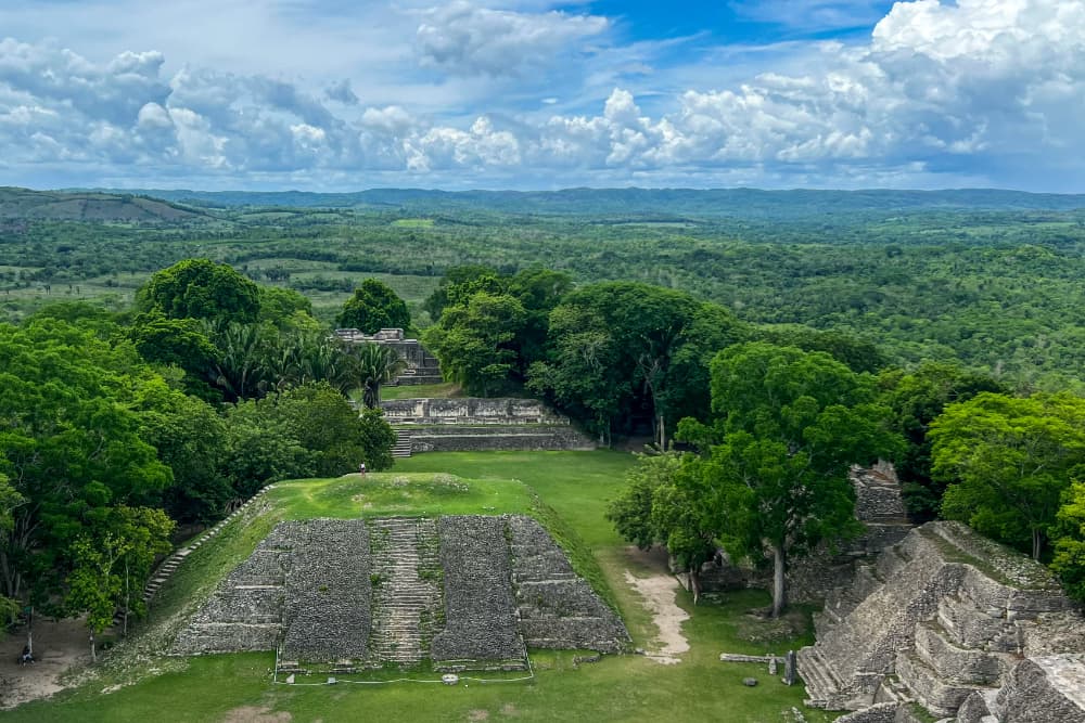 Aerial view of ancient stone ruins surrounded by lush greenery and distant mountains under a cloudy sky.