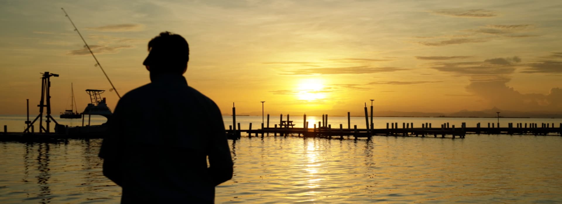 A silhouetted figure stands by the water as the sun sets, casting a warm glow over the landscape.