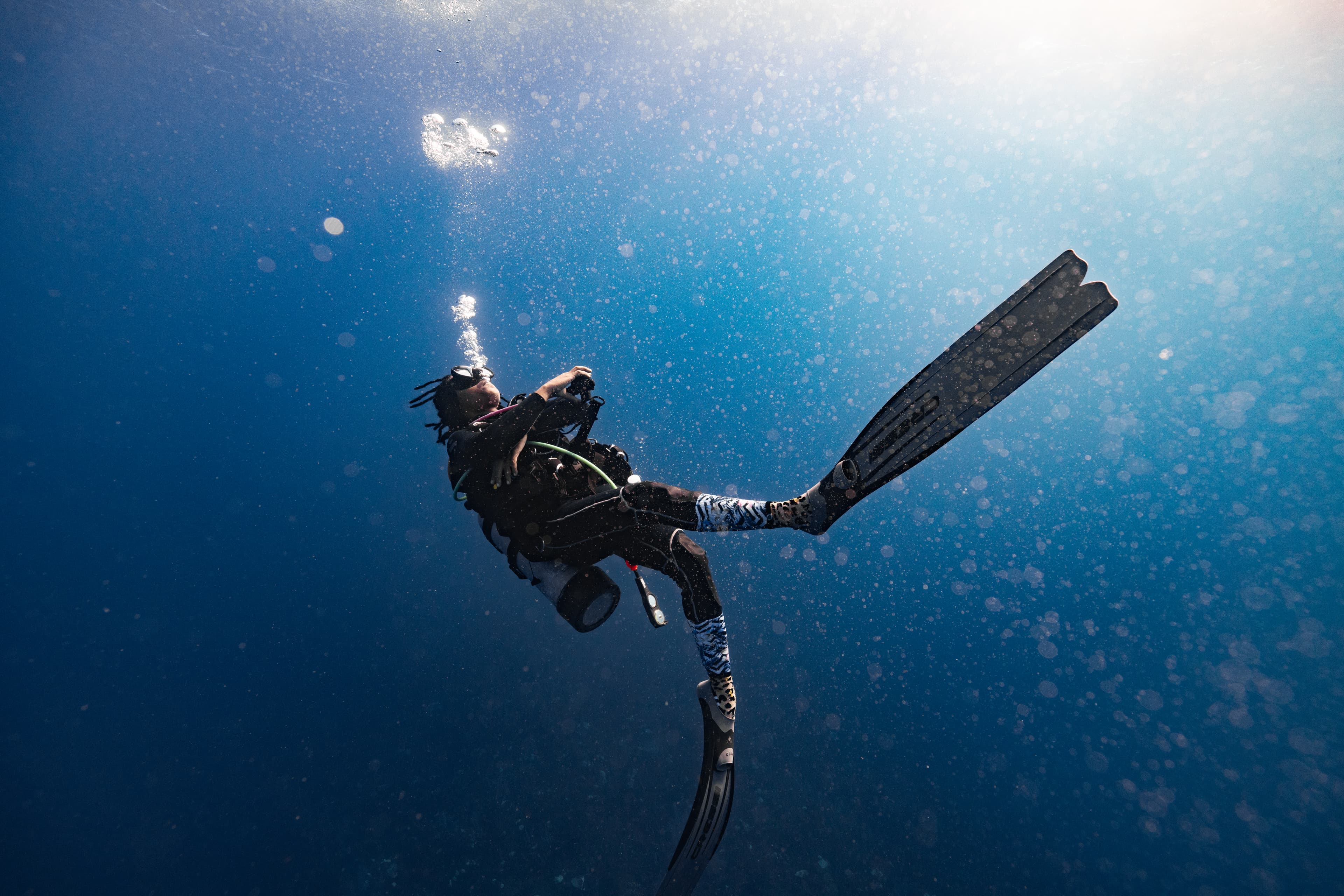 A diver swims upward in clear blue water, surrounded by bubbles.