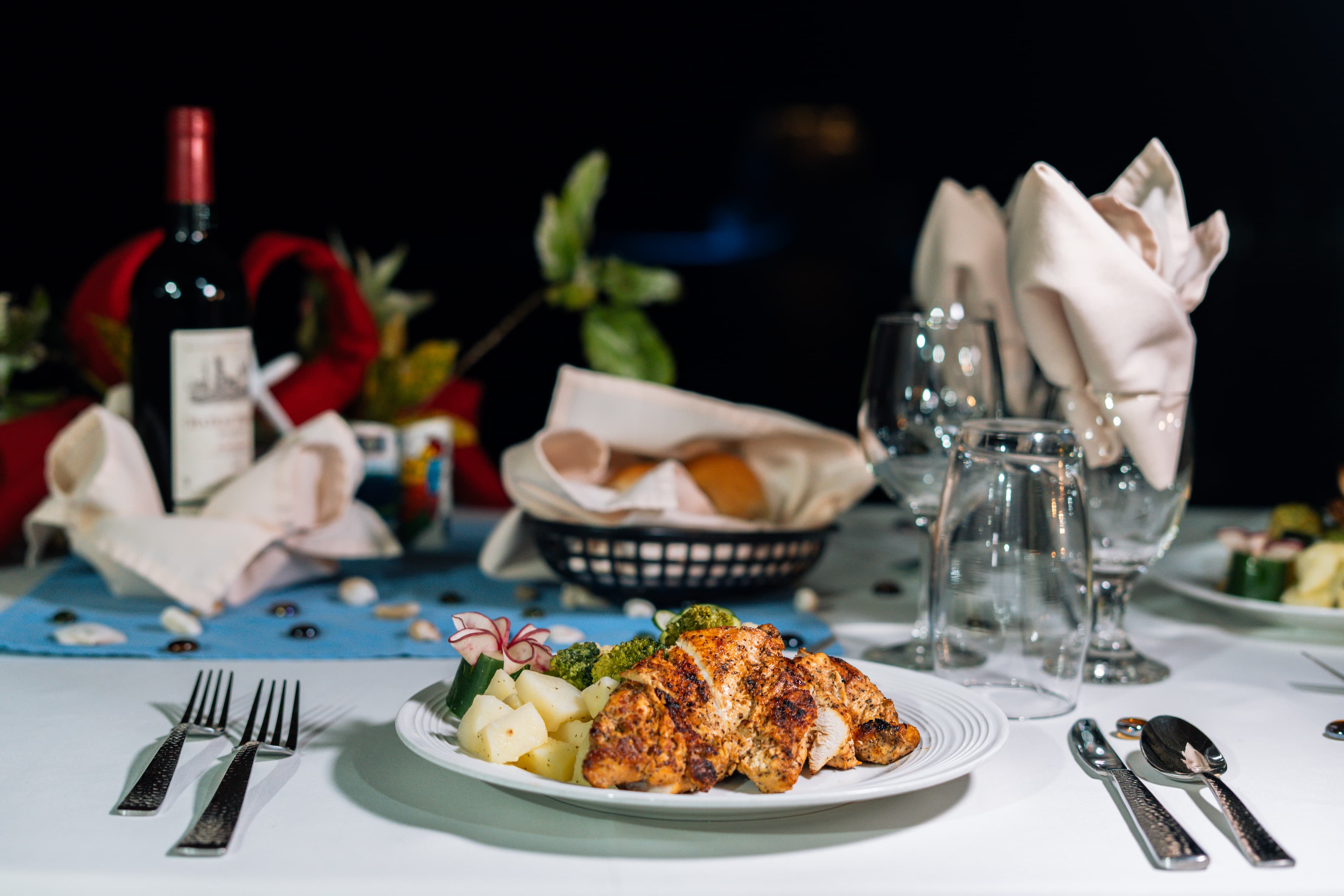 A beautifully set dining table featuring a plate of seasoned chicken, vegetables, and a glass of red wine.