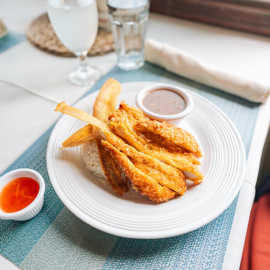 A plate of fried fish served with rice, plantains, and two dipping sauces.