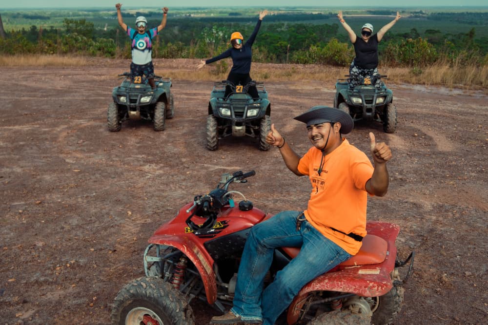 A group of four people celebrates on ATVs in a scenic outdoor setting.