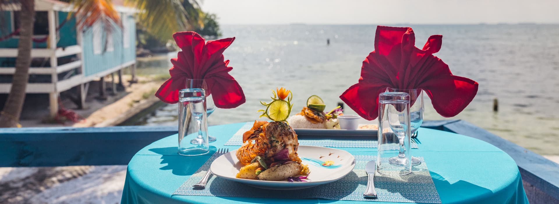 A beautifully set table with seafood, glasses, and red napkins, overlooking a serene seaside view.