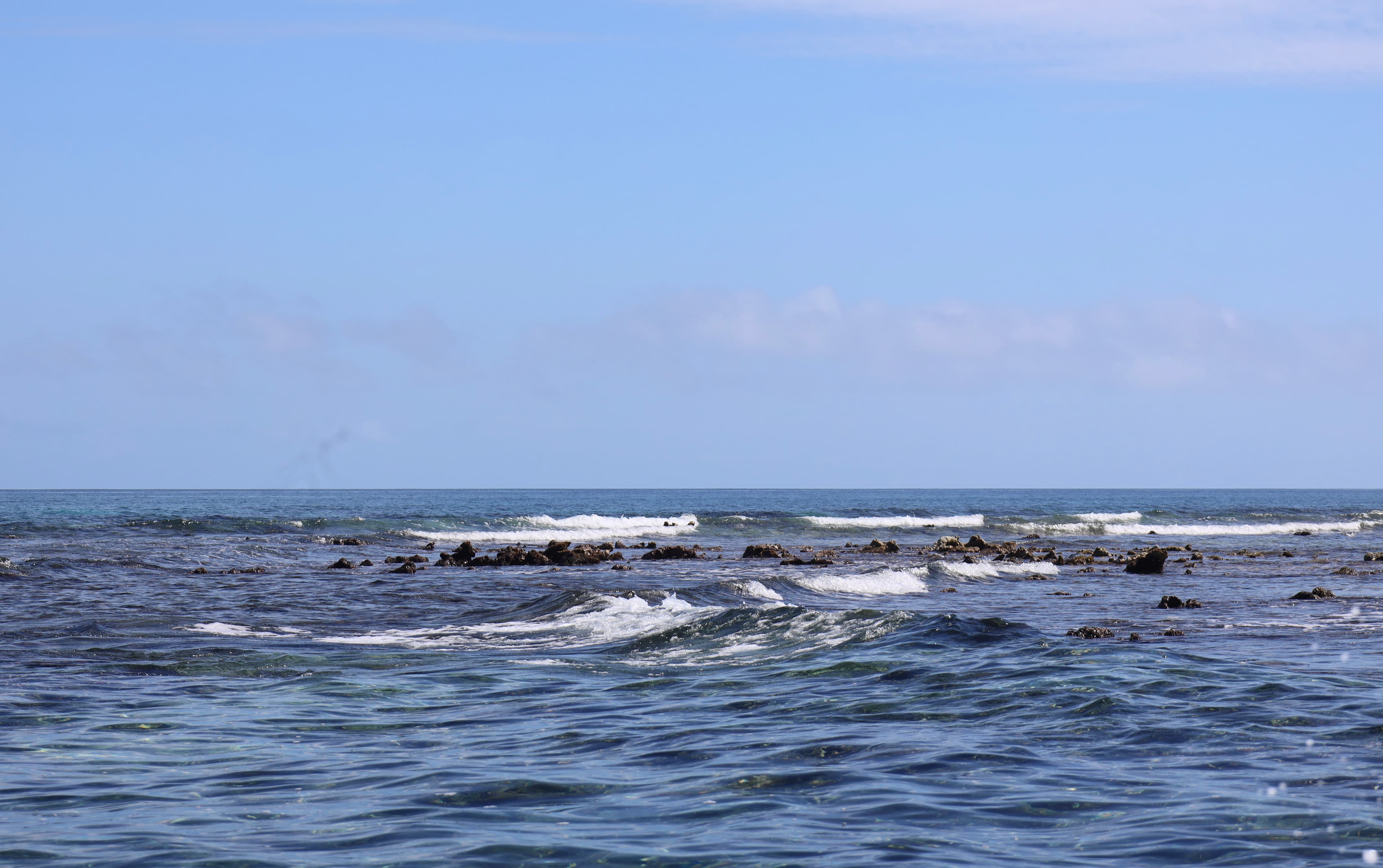 A tranquil ocean scene with gentle waves and rocky outcrops under a clear blue sky.