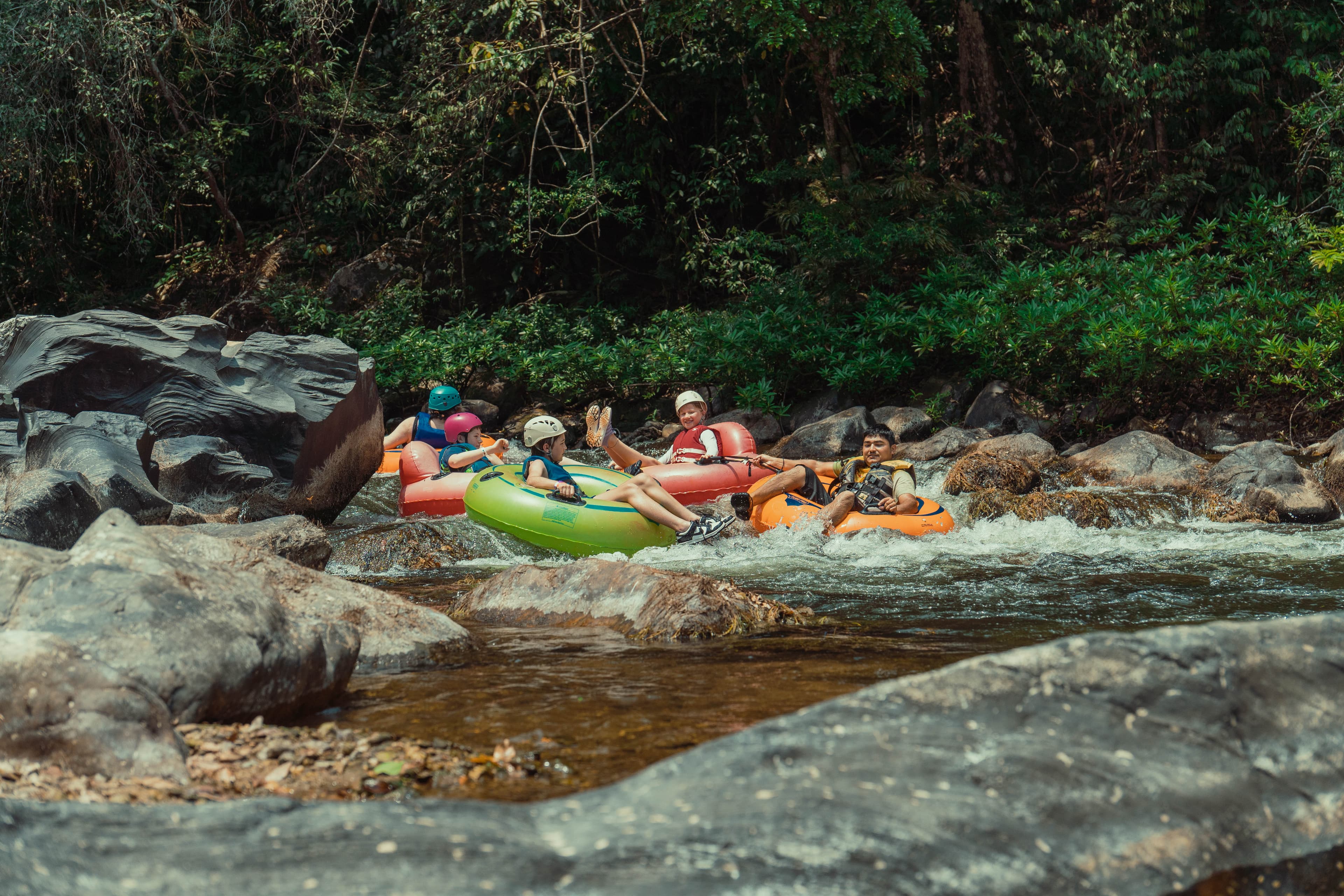 A group of people enjoy river rafting in colorful inflatables surrounded by lush greenery and rocks.
