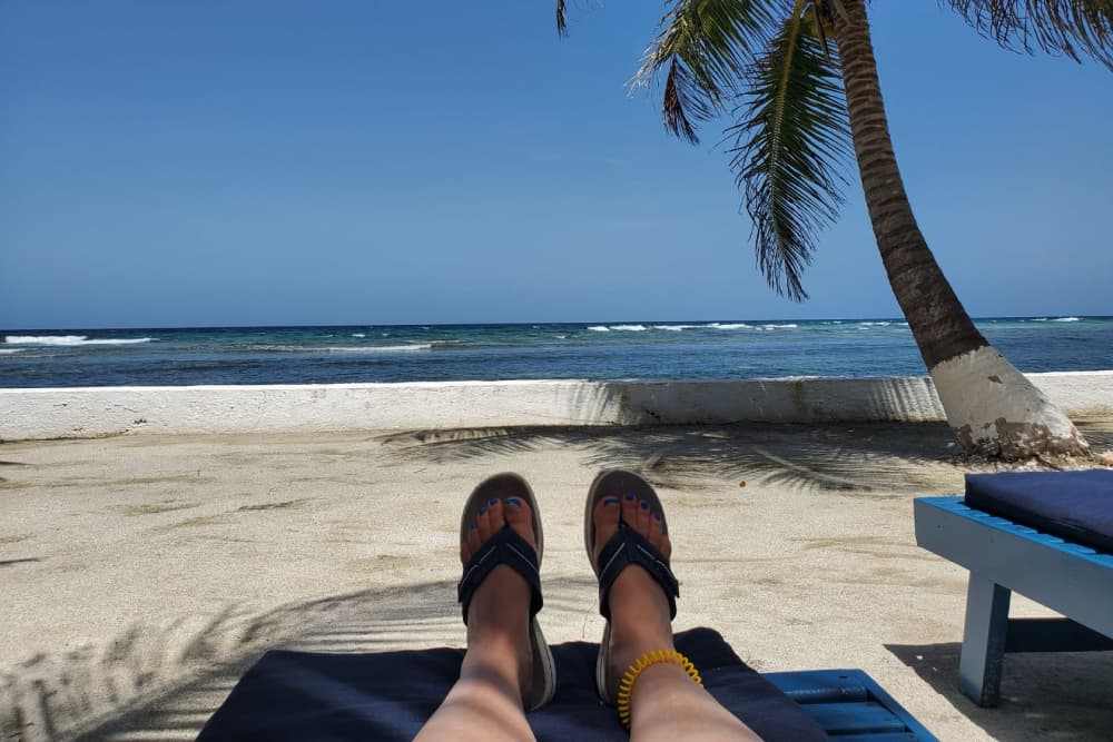 Feet in sandals resting on a beach lounge chair with ocean waves in the background.