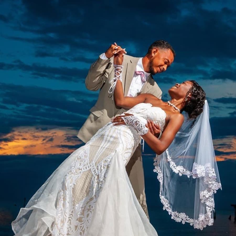 A groom dips his bride against a dramatic sunset backdrop.