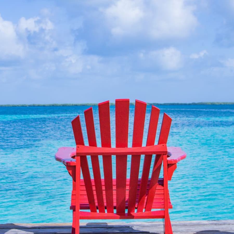 A bright red Adirondack chair faces a tranquil blue sea under a partly cloudy sky.