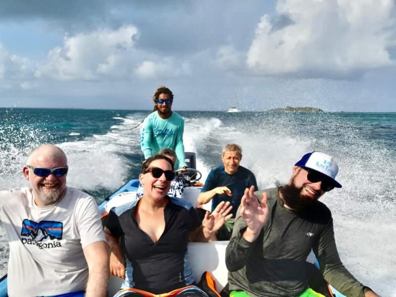 A group of five people enjoys a boat ride with smiles and waves against a backdrop of blue water and cloudy skies. A group of five people enjoys a boat ride with smiles and waves against a backdrop of blue water and cloudy skies.
