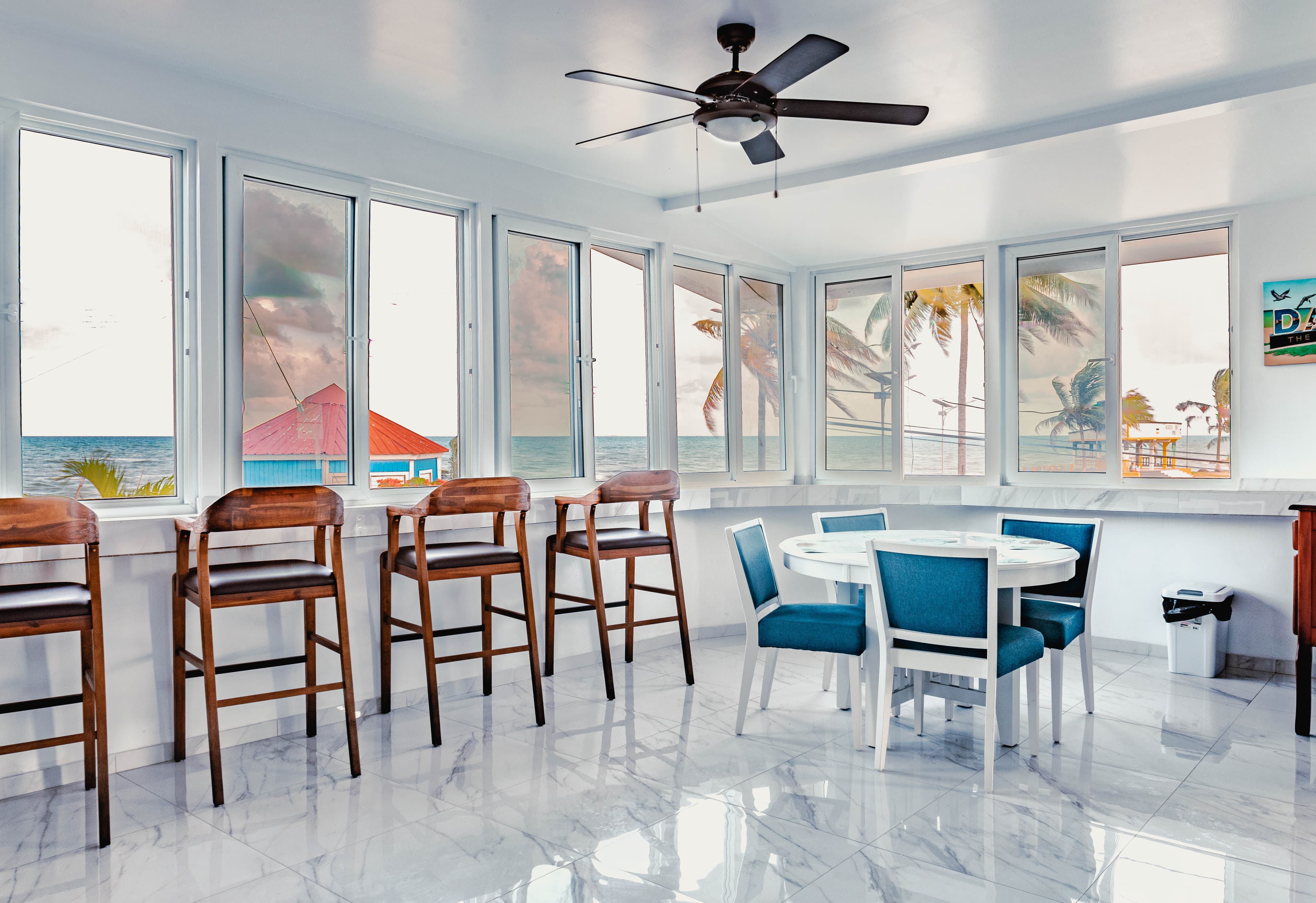 Bright interior dining area with coastal views through large windows, featuring wooden bar stools and a round dining table.