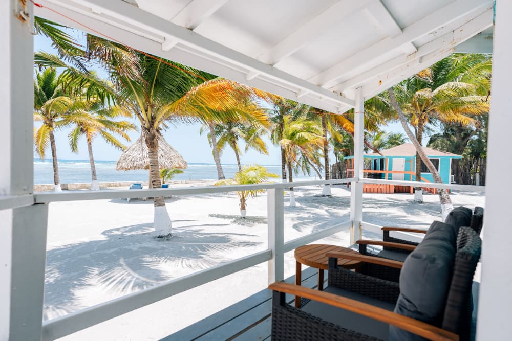 View from a beachside porch with palm trees and turquoise water in the background.