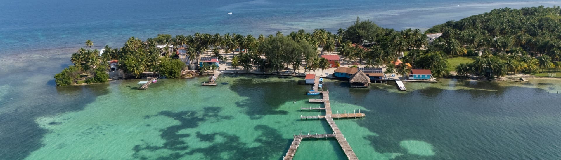 Aerial view of a tropical island with palm trees and dock leading to clear turquoise waters.
