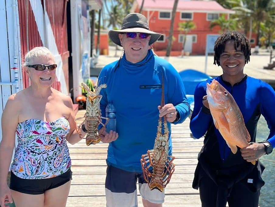 3 smiling people holding freshly caught lobsters and fish