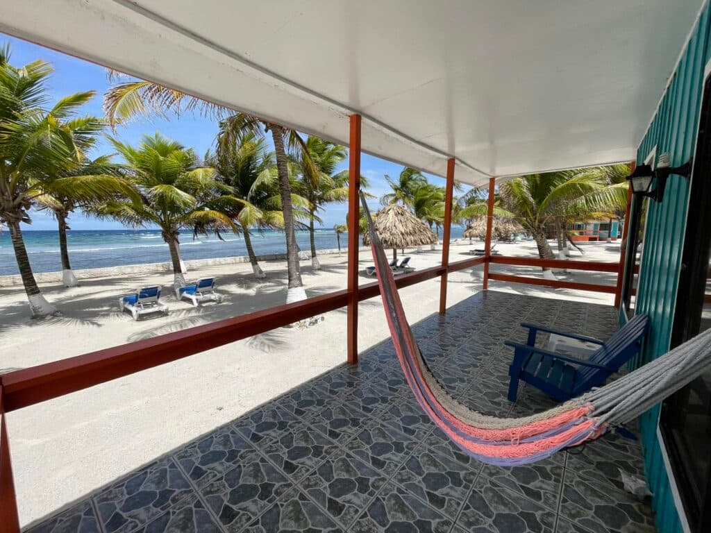 The terrace of a private cabana with a hammock, overlooking the white sand beach with palm trees, lounge chairs, and views of the beautiful Caribbean ocean.