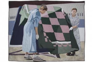 Two women displaying handmade quilts